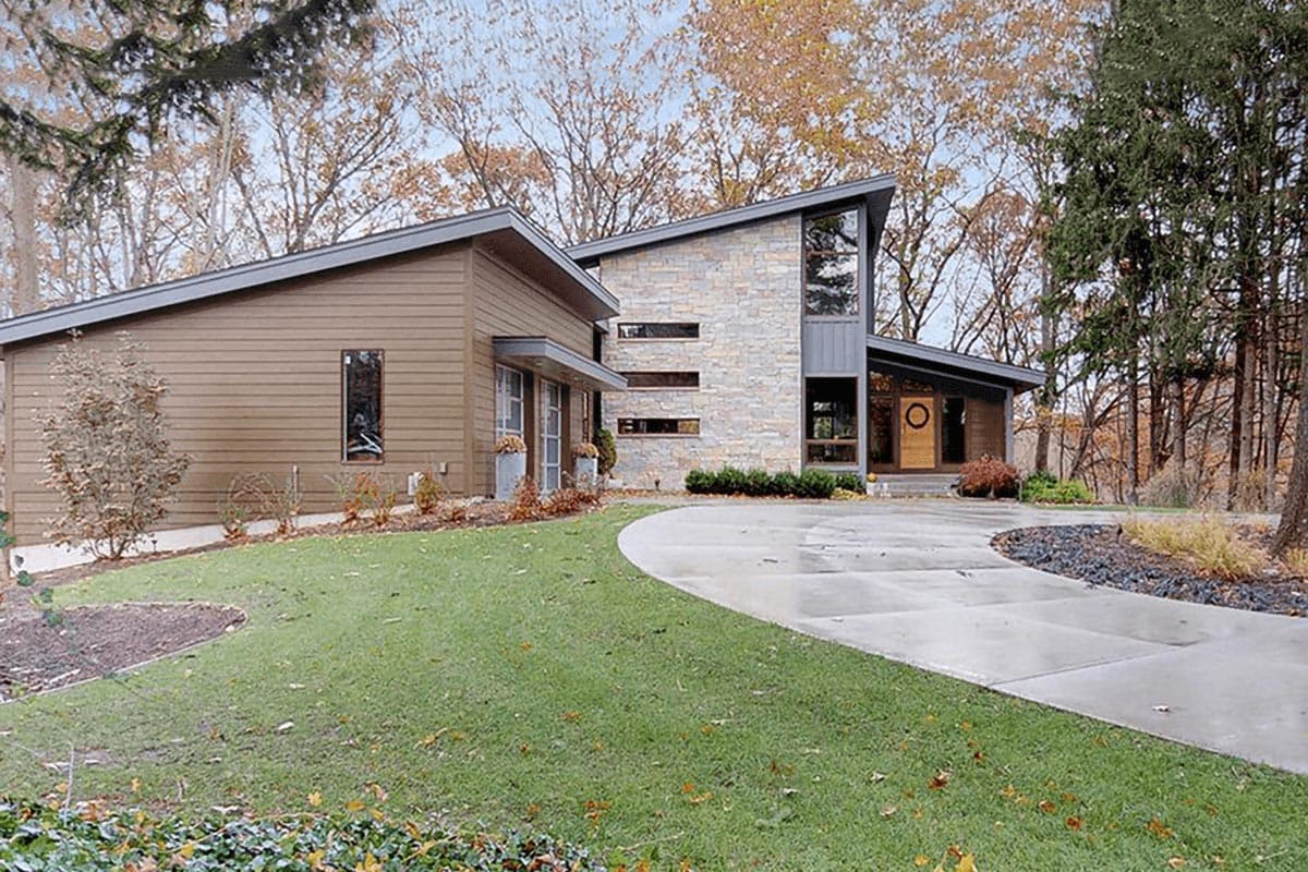 Modern house plan exterior with stone facade, asymmetric gables, and large vertical windows.