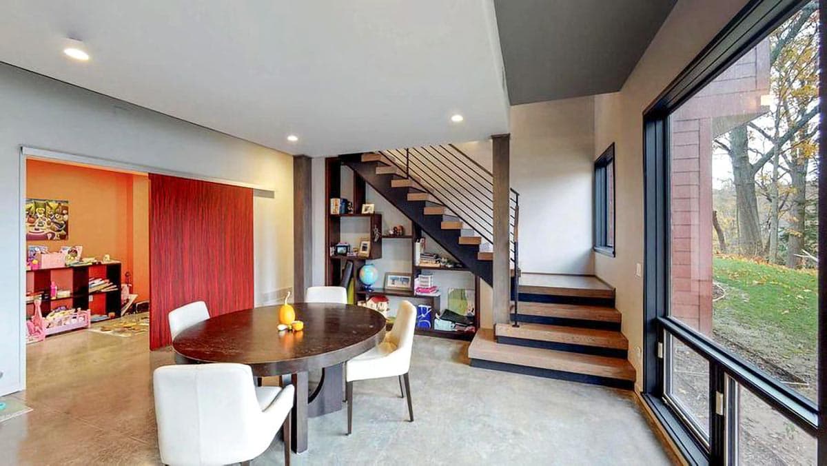 Interior view of a modern dining area with open staircase, large windows, and a sliding barn door to a playroom.