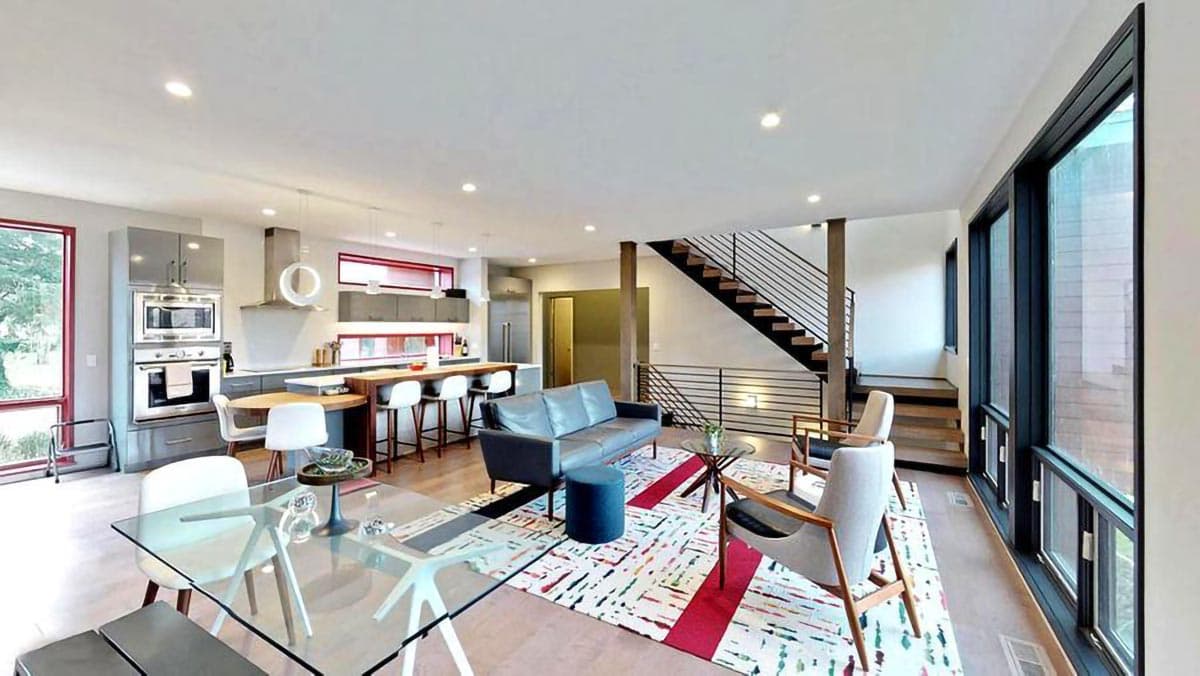 Modern open-plan living space with kitchen, dining, and seating areas, featuring a sleek staircase and large windows.