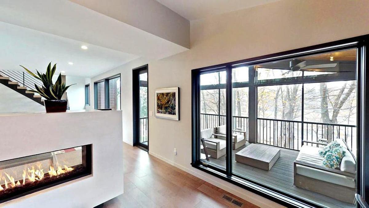 Interior view showing a modern living area with a linear fireplace, stairs, and large sliding glass doors leading to an outdoor seating area.