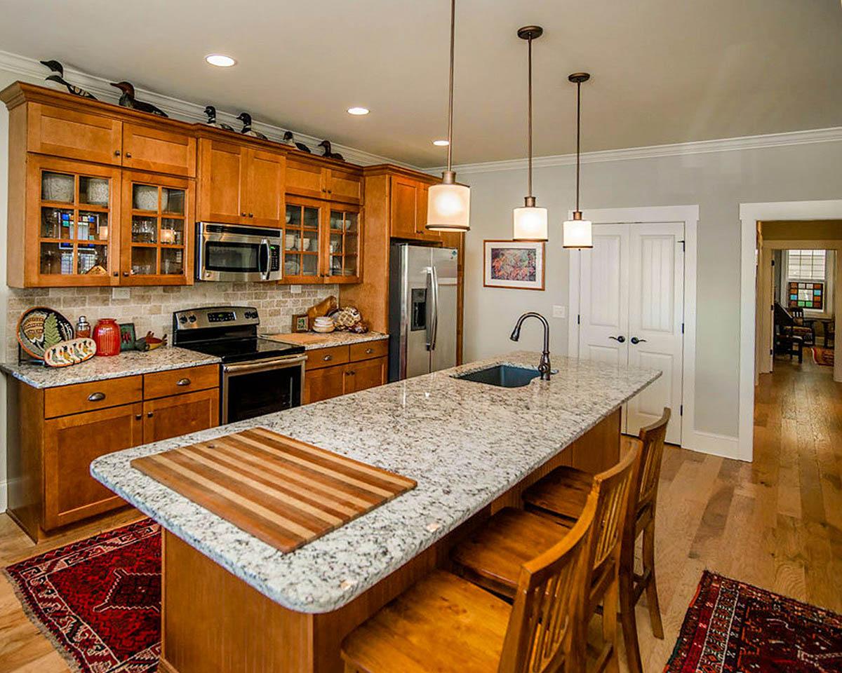 Kitchen with wood cabinetry, granite island with sink and pendant lights, stainless steel appliances, and a view of adjacent dining area.