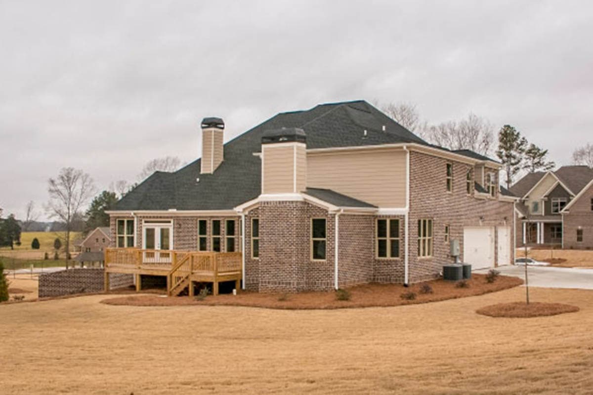 House plan exterior: Two-story brick home with a large wooden deck, dual garage doors, and prominent chimneys.