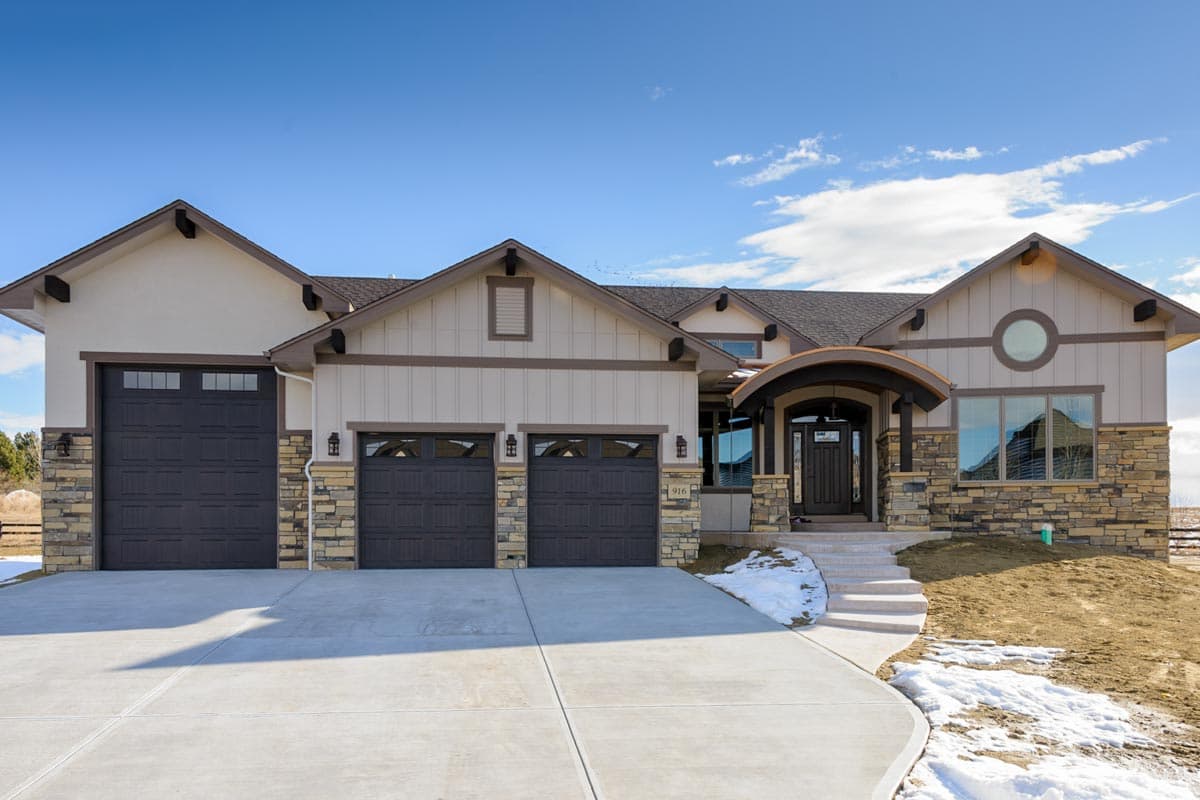 House plan exterior. One-story house with gabled roof, stone accents, and a covered entry porch. Features three garage doors.