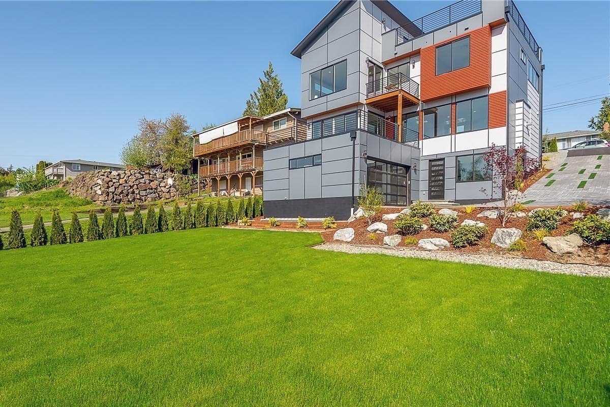 Modern house plan exterior with multiple stories, balconies, gray paneling, and an orange accent.
