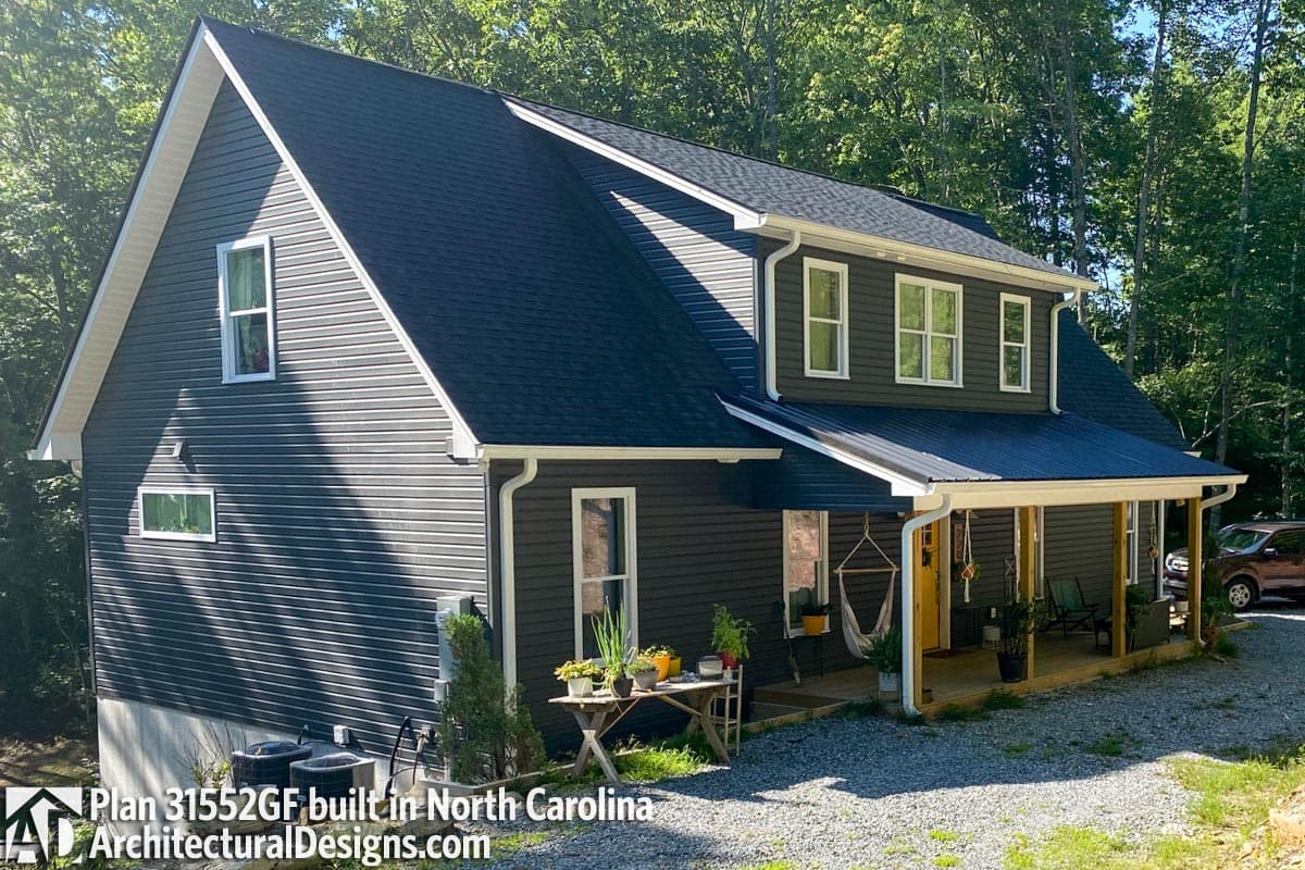 Two-story house plan exterior with dark siding, white trim, multiple gables, and a wraparound porch.