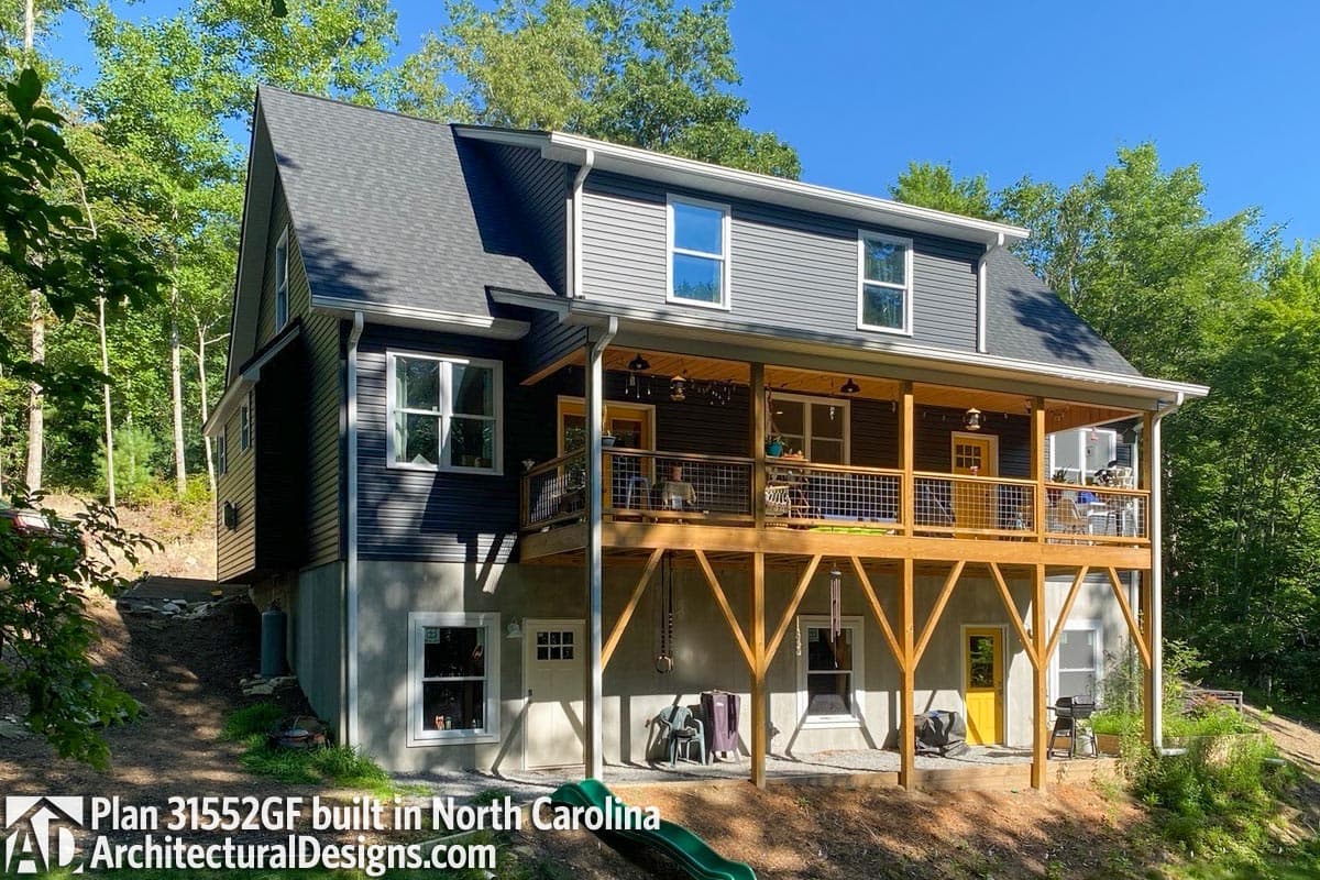 House plan exterior: Two-story modern design with a prominent gable roof, second-story deck, and exposed wood support beams.