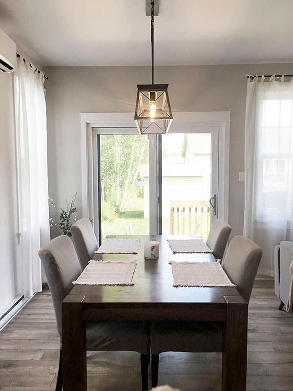 Dining area with dark wood table, upholstered chairs, and a modern industrial pendant light over a sliding glass door.