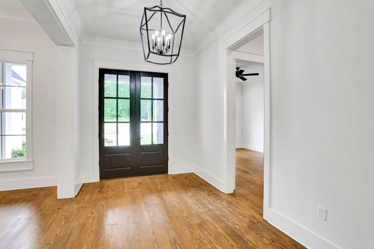 Interior view of a hallway with dark double doors, wood floors, and a geometric pendant light.