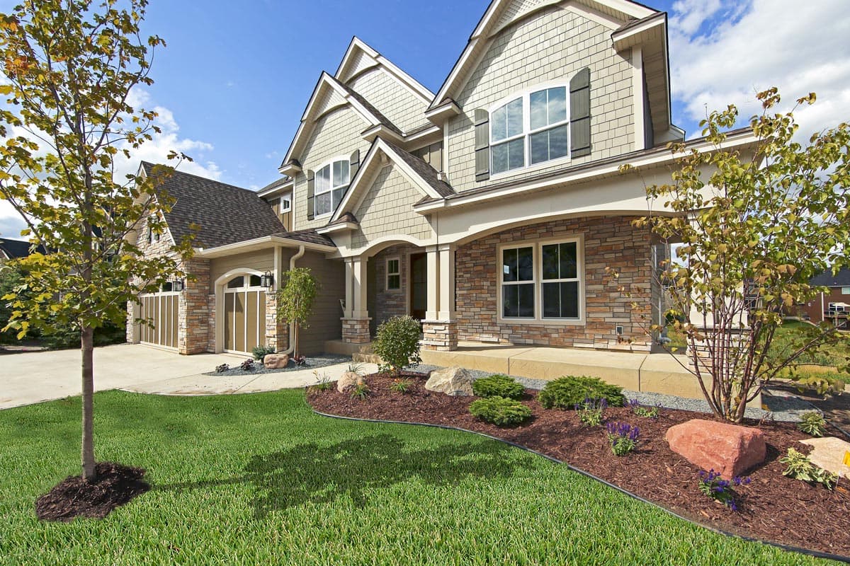 Two-story house plan exterior with stone accents, covered entry porch, arched garage doors, and multiple gables.