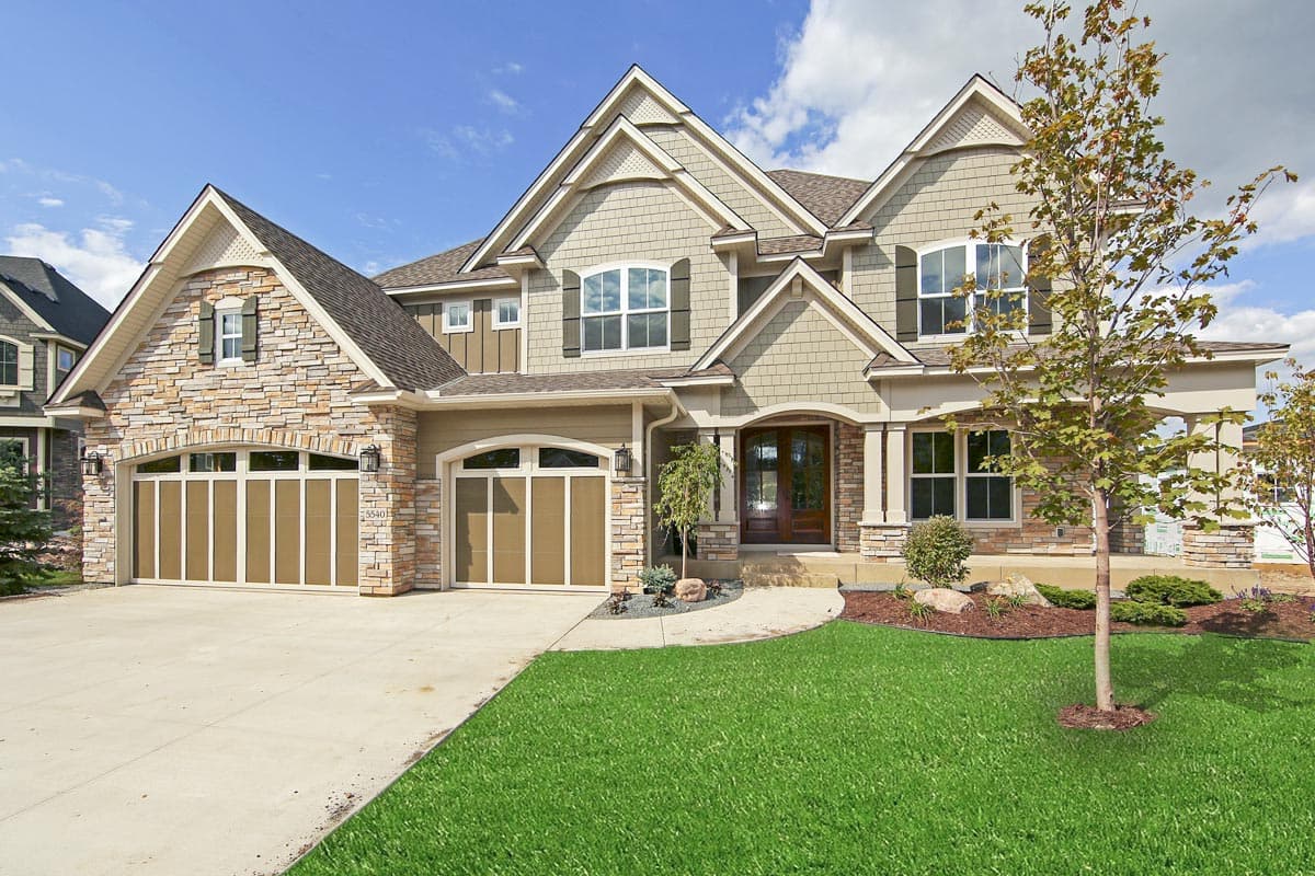 House plan exterior. Two-story Craftsman home with a stone facade, gabled rooflines, and a front-facing, three-car garage.