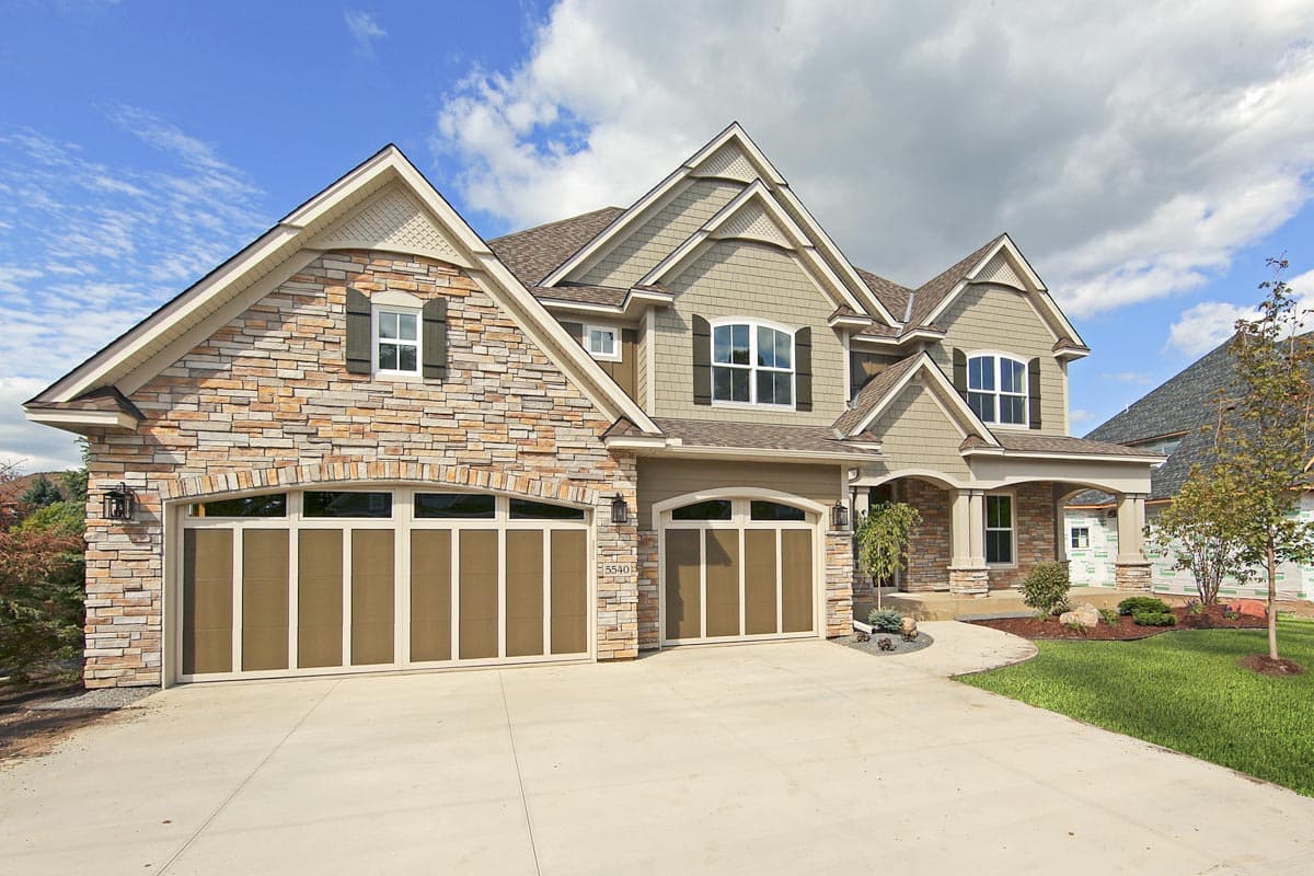 House plan exterior with stone accents, multiple gables, and a three-car garage with arched doors.