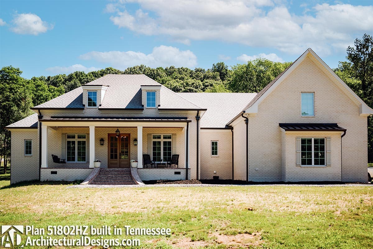 House plan exterior: One-story Modern Farmhouse with a wide covered porch, brick construction, and dormer windows.