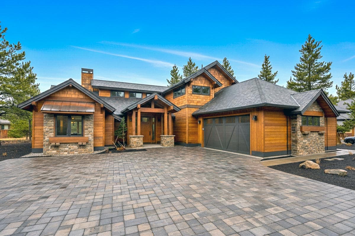 House plan exterior showing a two-story modern lodge-style home with wood siding, stone accents, covered entry, and attached garage.