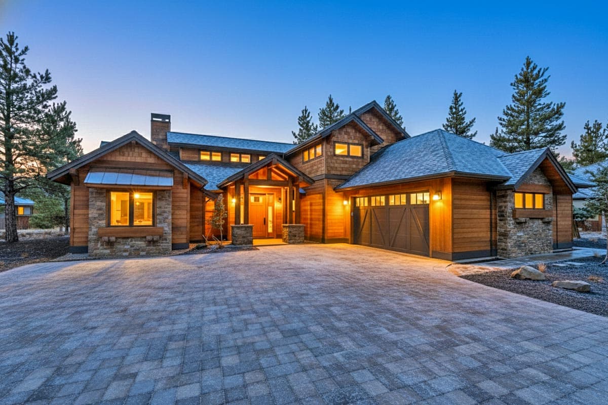 House plan exterior: Two-story modern mountain home with wood and stone facade, prominent gables, covered entryway, and attached two-car garage.