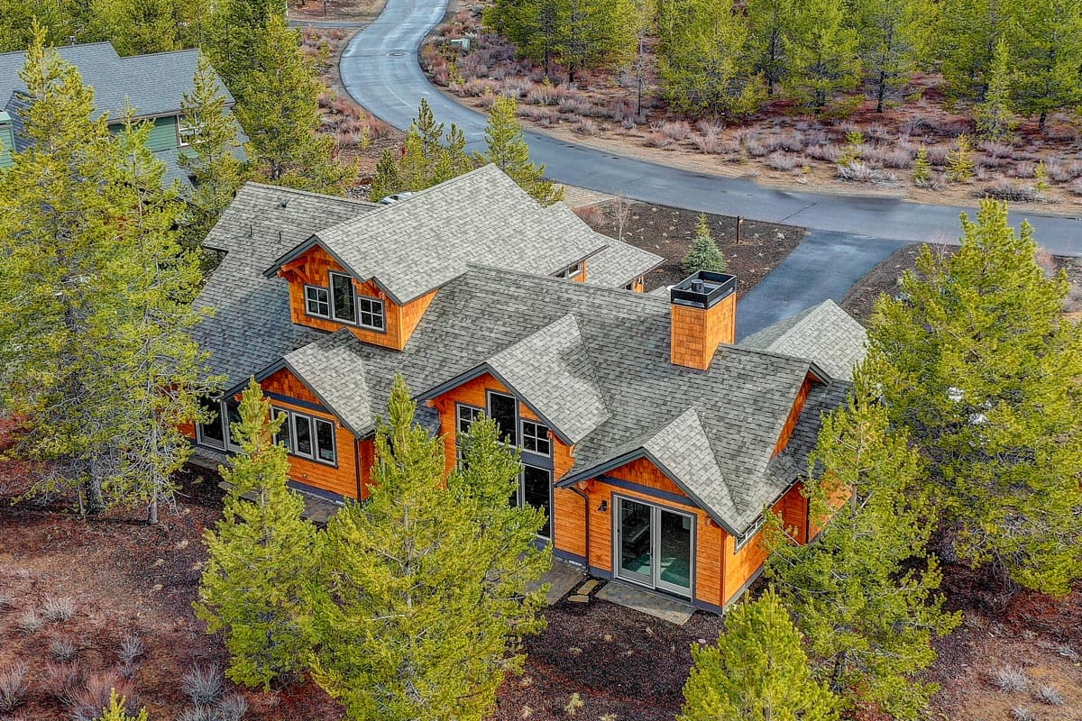 House plan exterior showing a multi-story home with wood siding, multiple gables, dormers, and a prominent chimney.