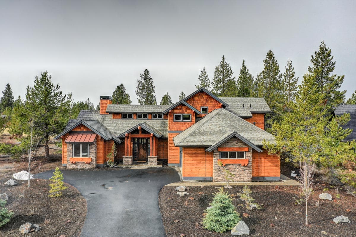 House plan exterior: Two-story home with wood siding, stone accents, prominent gables, and covered entry.