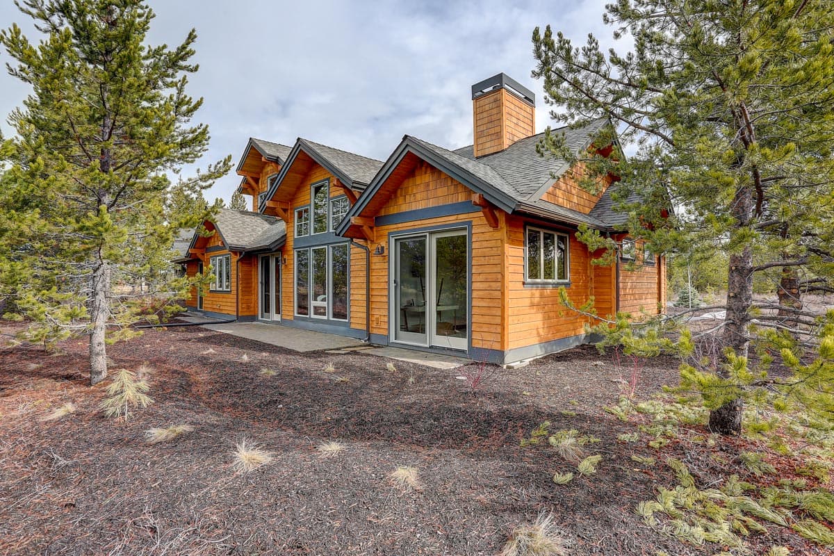 Modern wood-sided house plan with multiple gables, large windows, and a prominent stone chimney.