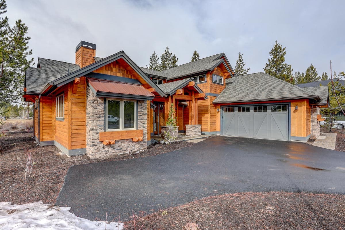 Modern mountain house plan exterior with wood siding, stone accents, multiple gables, and a two-car garage.