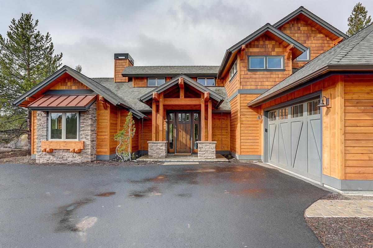 House plan exterior: Modern mountain style with wood siding, stone accents, prominent gables, a covered entryway, and a two-car garage.