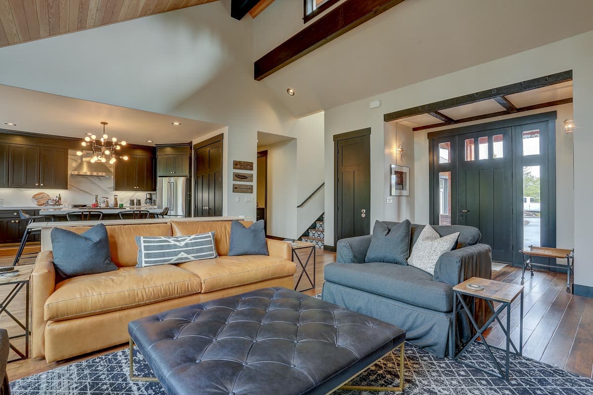 Living room with vaulted ceiling, exposed beams, leather sofa, and dark entry doors. Open to kitchen with island.