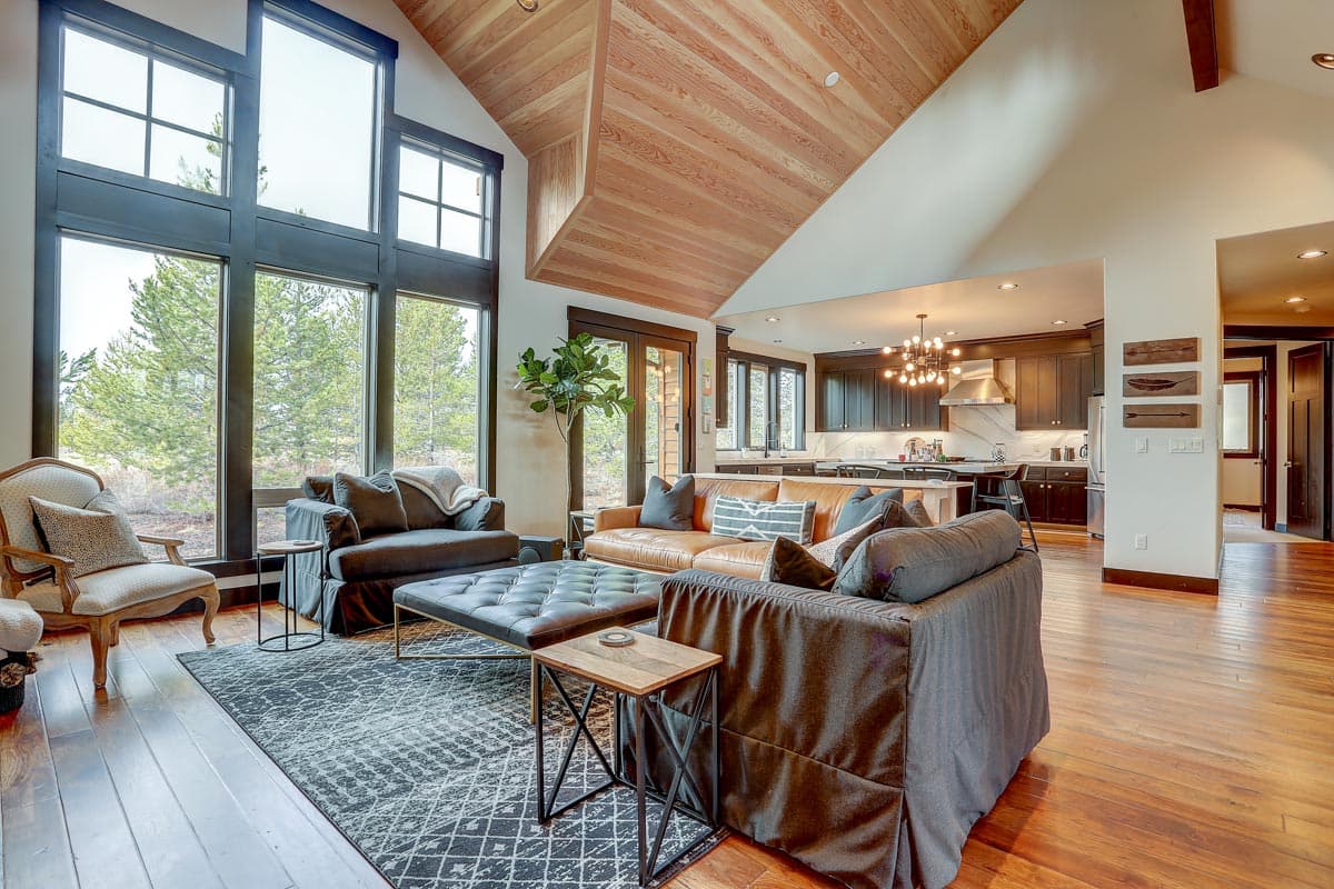Interior view of great room with vaulted wood ceiling, floor-to-ceiling windows, and open kitchen with island.