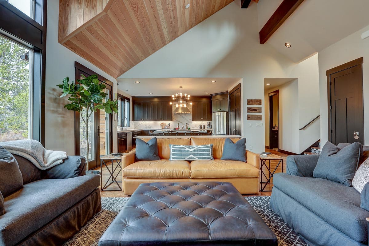 Living room with vaulted wood-paneled ceiling, leather sofa, and open kitchen with dark cabinetry.