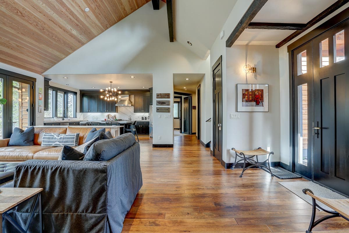 Interior view of an open-concept home with vaulted wood-paneled ceiling, dark kitchen cabinetry, and seating area.