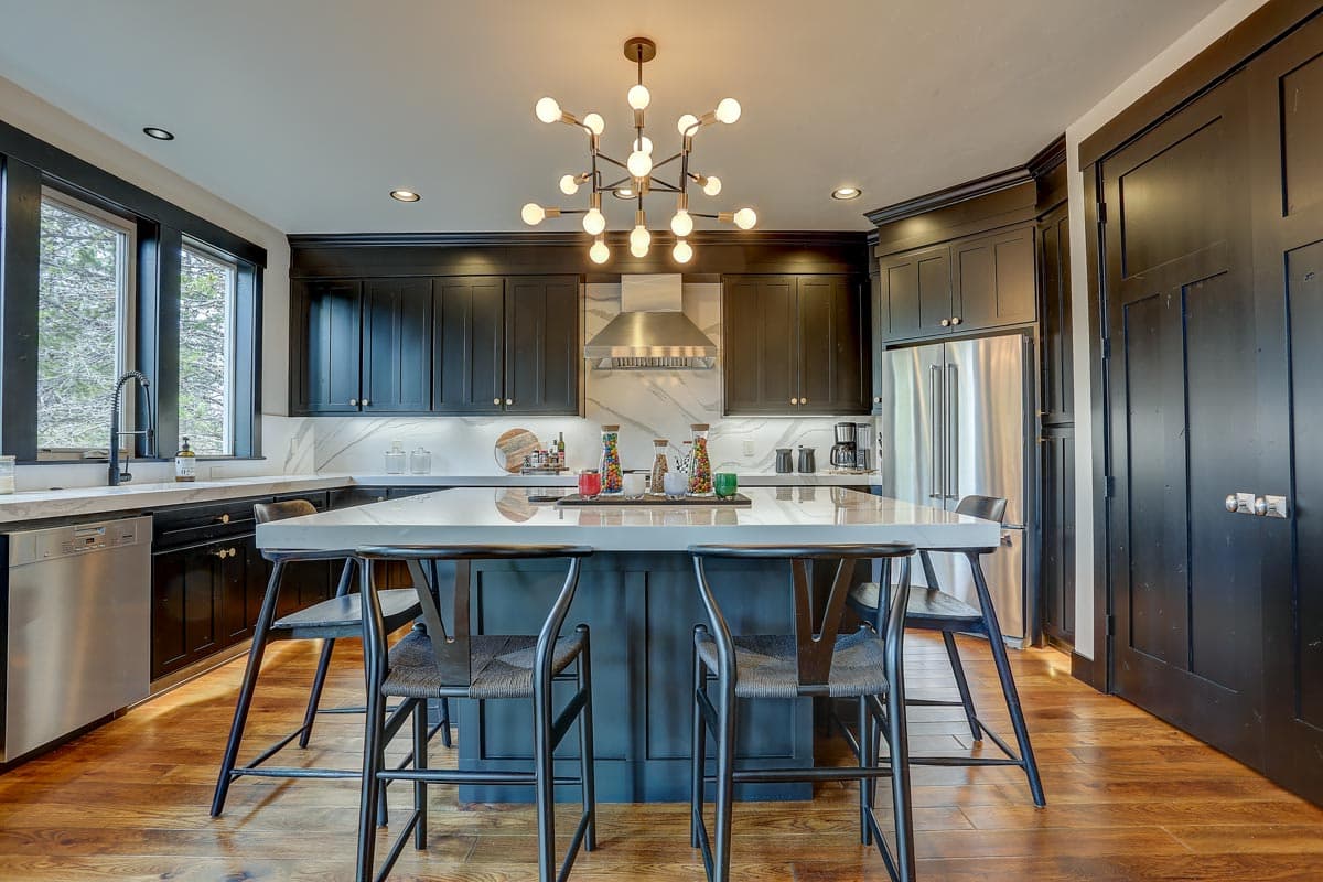 Kitchen with dark cabinetry, large island with seating, stainless steel appliances, and modern chandelier.