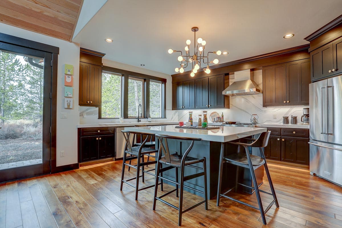 Kitchen with dark cabinets, large island with seating, stainless steel appliances, and view to wooded exterior.