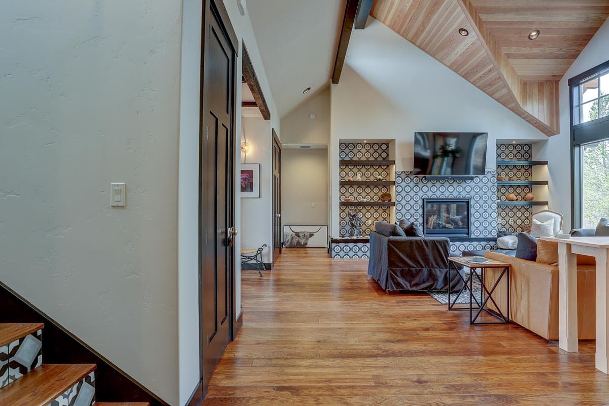 Living room with vaulted wood ceiling, fireplace, built-in shelves, and large windows.