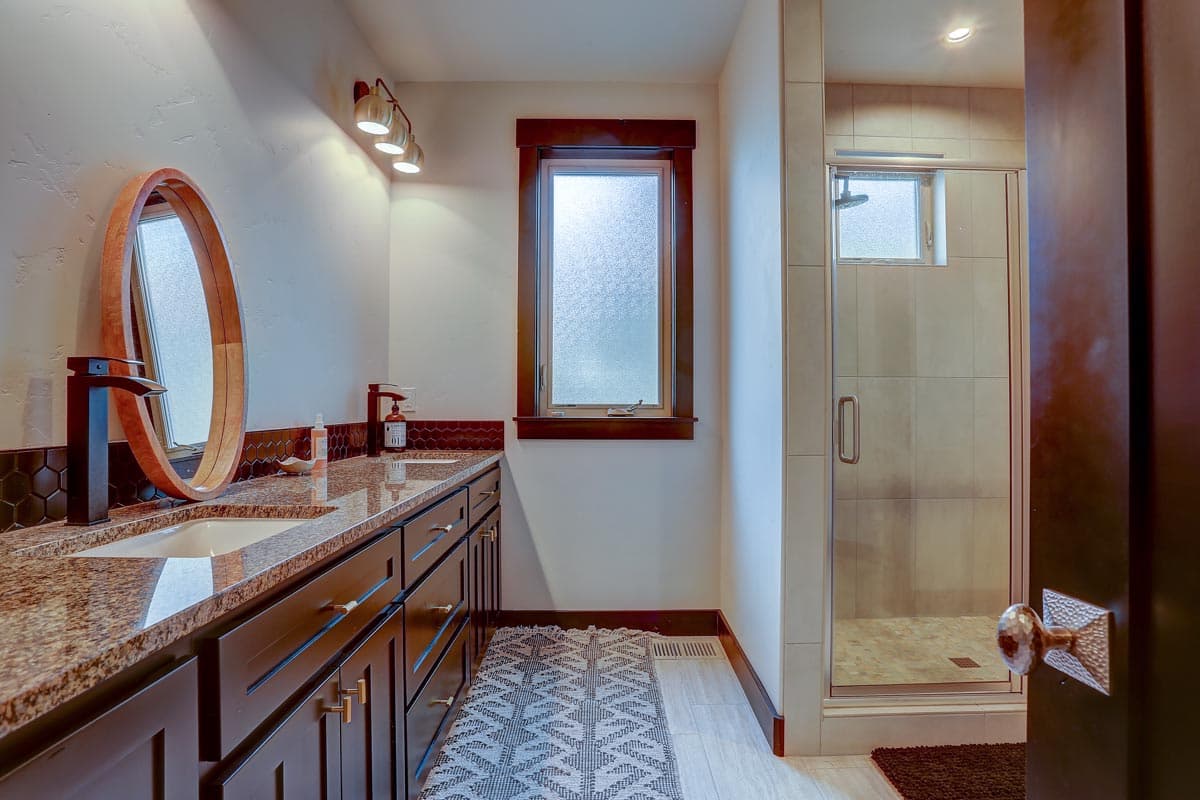 Bathroom with dual sinks, granite countertops, dark wood vanity, and glass-enclosed shower.