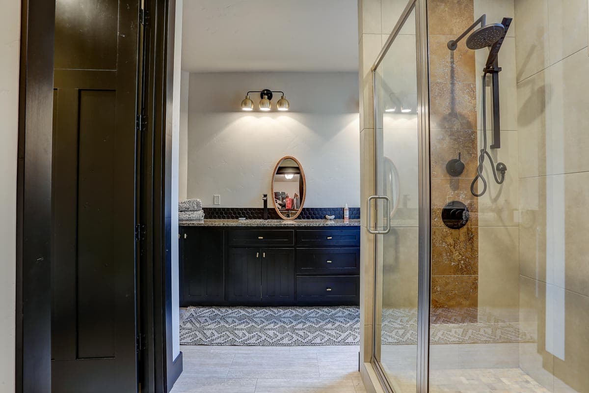 Bathroom with black vanity, granite countertop, oval mirror, and glass-enclosed shower with tiled walls.