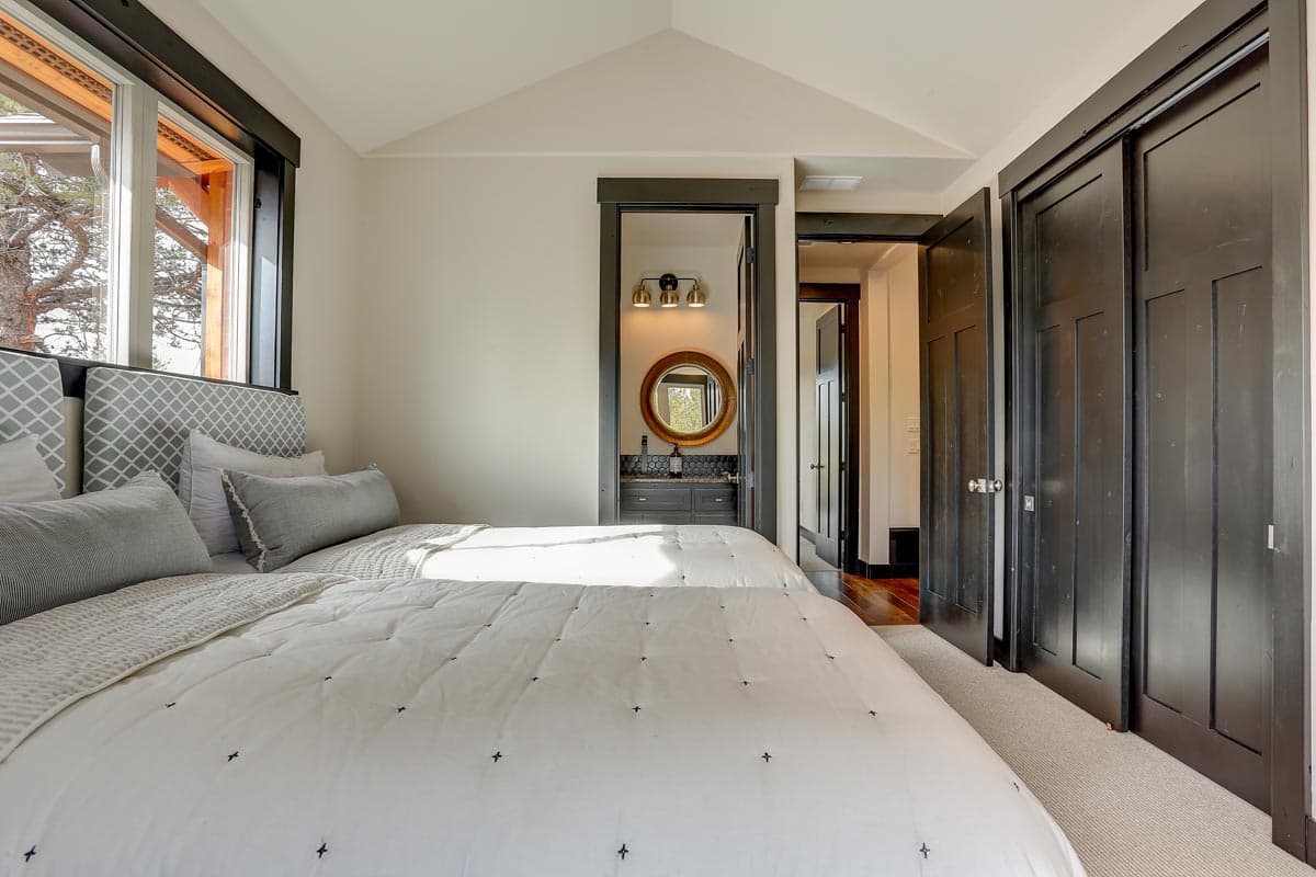 Bedroom with two beds, pitched ceiling, large window, ensuite vanity, and dark wood doors.