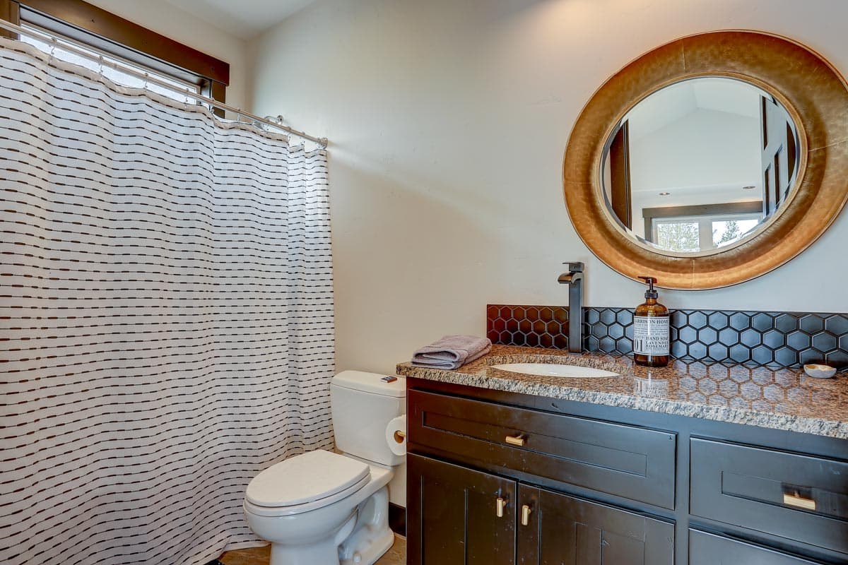Bathroom interior with shower curtain, toilet, vanity with granite countertop, sink, and round mirror.