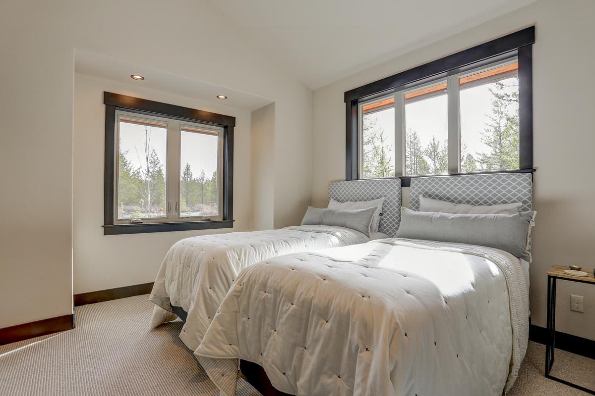 Bedroom interior with two twin beds, patterned headboards, and large windows framing a forest view.