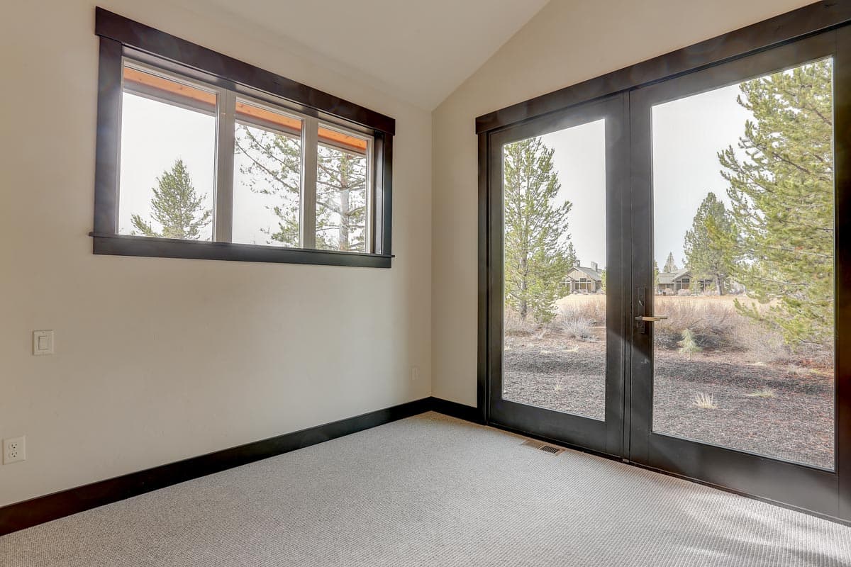 Interior view showing a room with a horizontal window and double glass doors opening to an exterior landscape with houses.