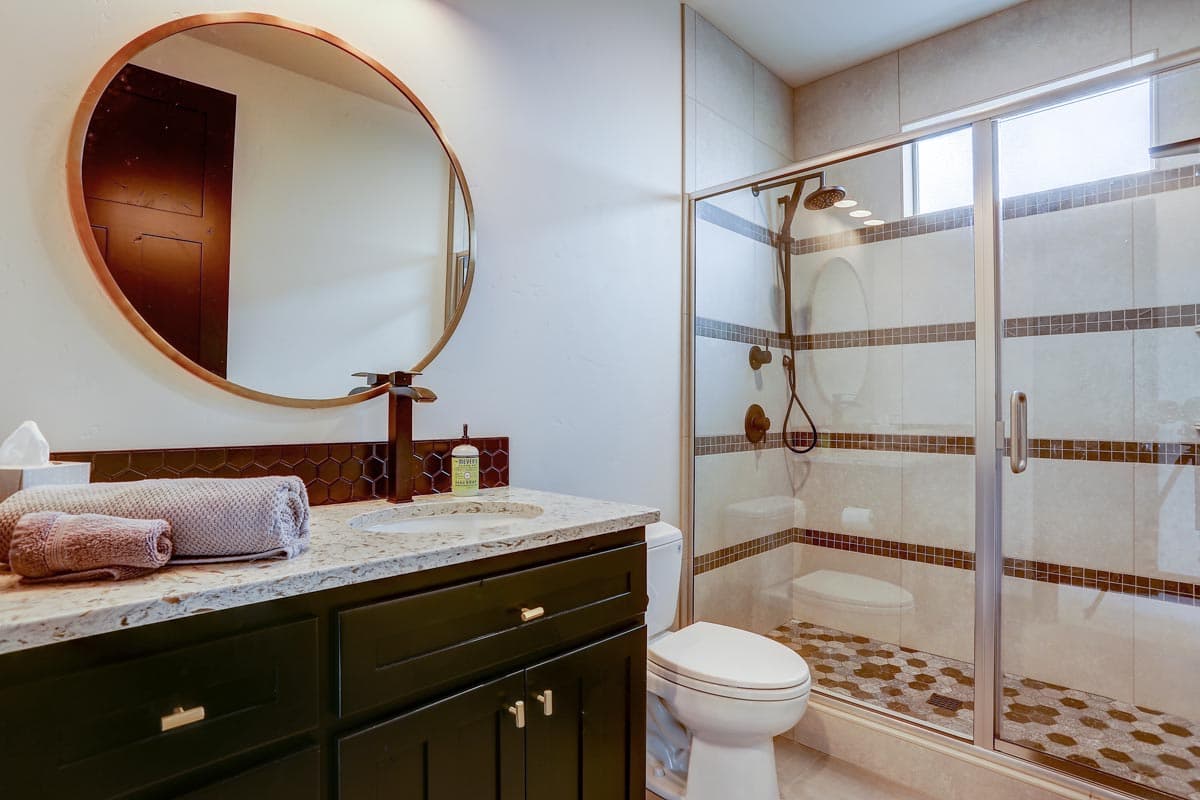 Bathroom with vanity, toilet, and glass-enclosed shower with tiled walls and hexagonal floor tiles.