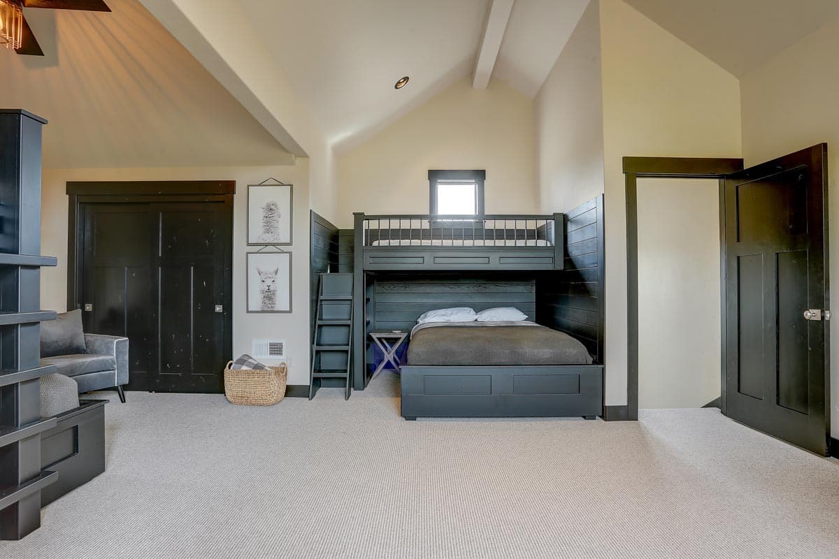 Bedroom with bunk beds, vaulted ceiling, dark wood paneled wall, sliding closet doors, and a ceiling fan.