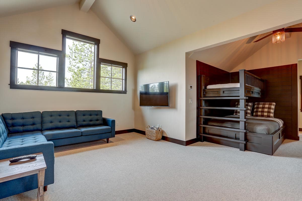 Interior view of a room with a blue sectional sofa, mounted TV, built-in bunk beds, and multiple windows.