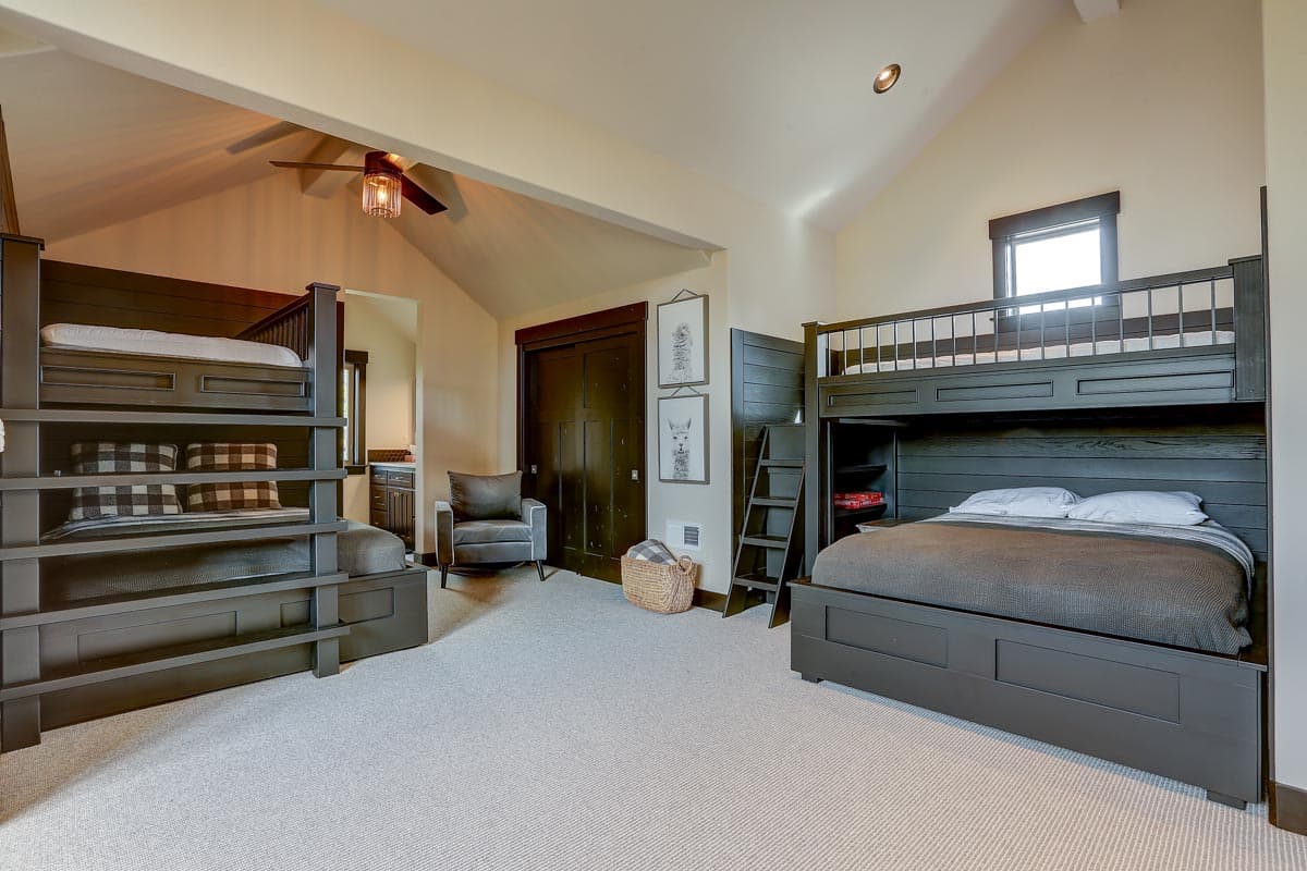 Interior view of bedroom with two bunk beds, a single bed, armchair, and vaulted ceiling.