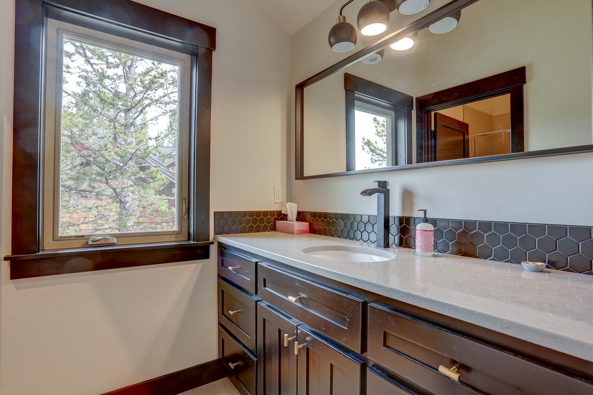 Bathroom vanity with dark wood cabinets, white countertop, undermount sink, black faucet, and hexagonal tile backsplash.