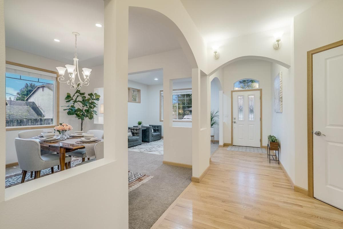 Interior view of a house with a dining area, living room, and entryway featuring arched openings and a glass-paneled front door.