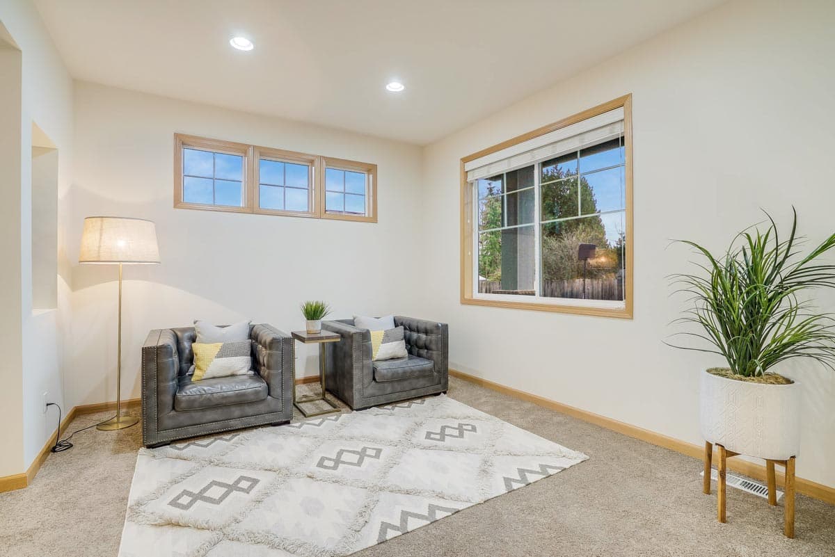 Interior view of a living space with two leather chairs, a patterned rug, recessed lighting, and large windows.