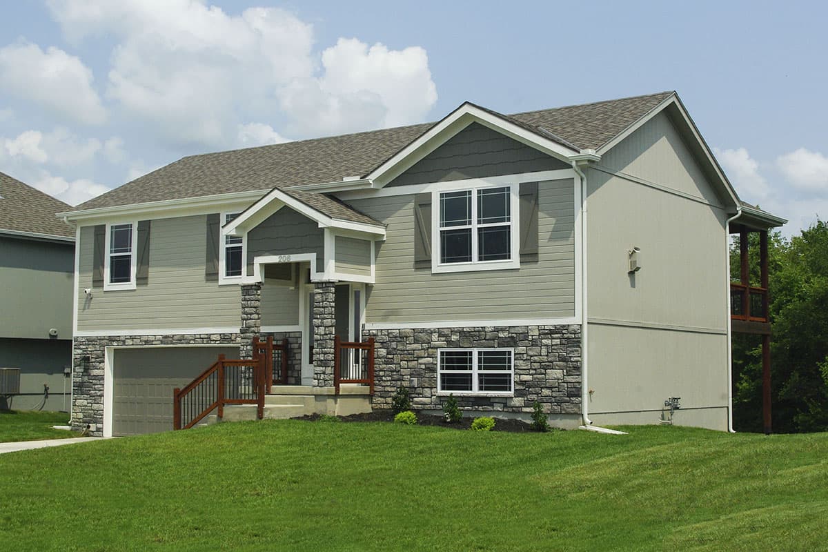 Two-story house plan exterior with stone base, siding, covered porch, gabled dormers, and attached garage.