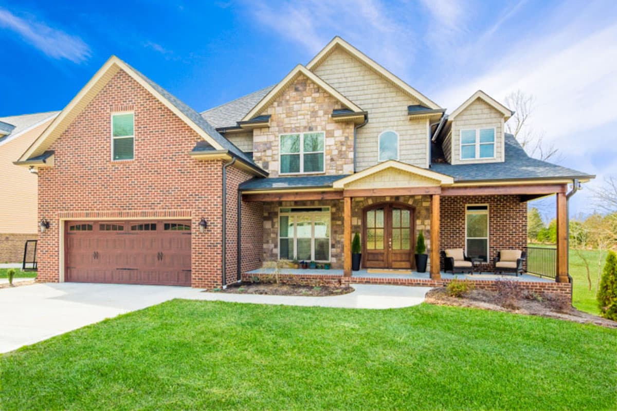 House plan exterior: Two-story brick home with stone accents, gables, front-facing garage, and covered front porch.