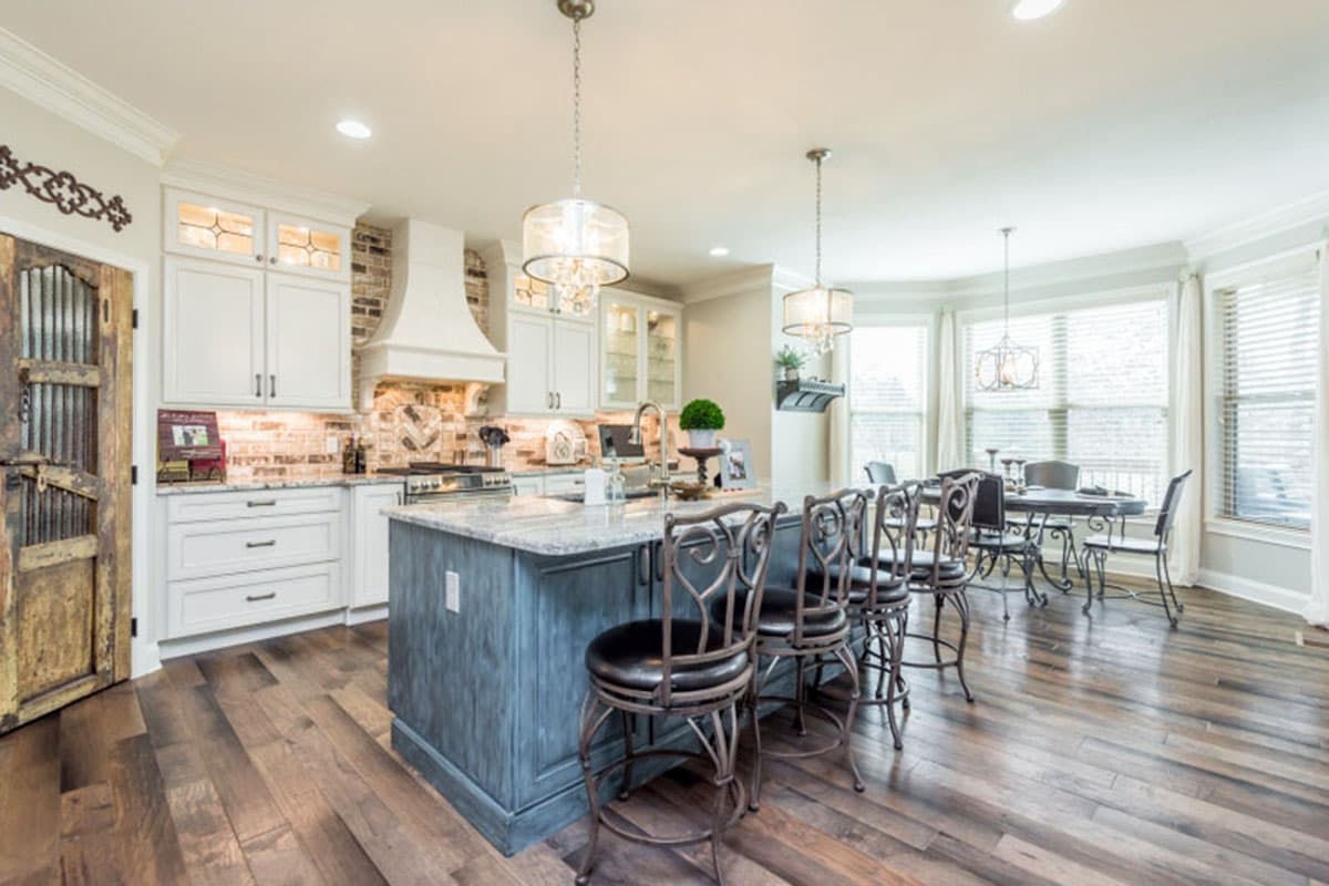 Kitchen with island seating, white cabinets, brick backsplash, stainless steel appliances, and dining area with large windows.