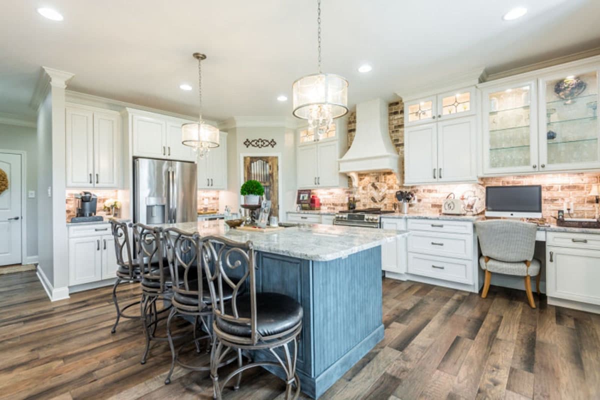 Kitchen with white cabinets, large island with seating, stainless steel refrigerator, range hood, and a built-in desk.