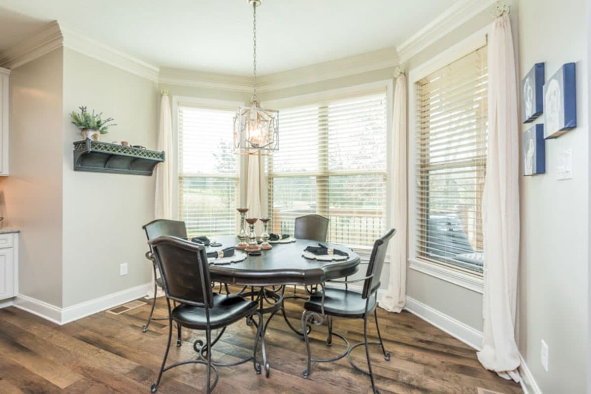 Dining room with oval table, chairs, bay windows, decorative shelf, and modern chandelier.
