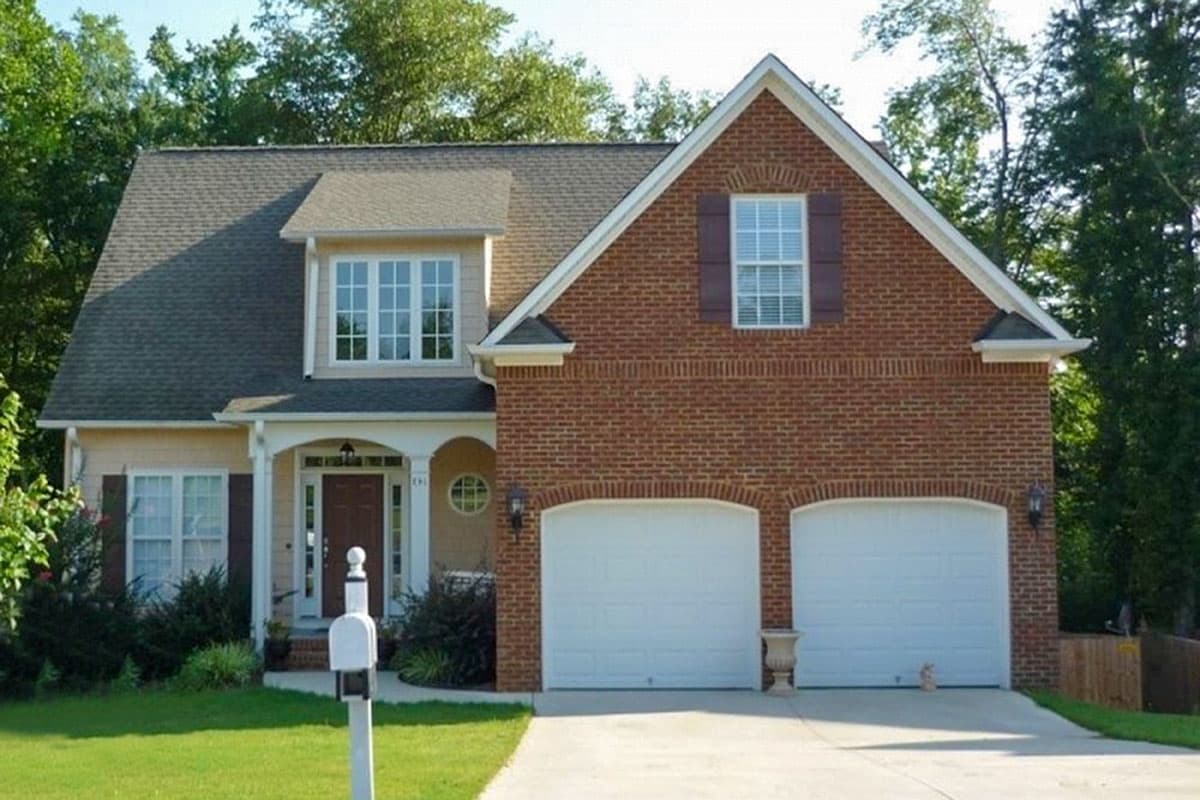 House plan exterior: Two-story home with brick facade, dual garage doors, covered porch with columns, and dormer window.