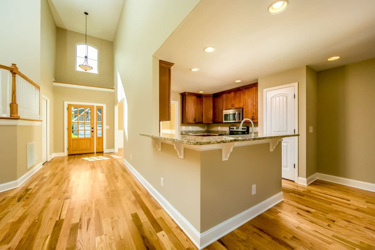 Interior view showing vaulted entryway with wood floors, double glass door, kitchen island with granite countertop, and wood cabinets.